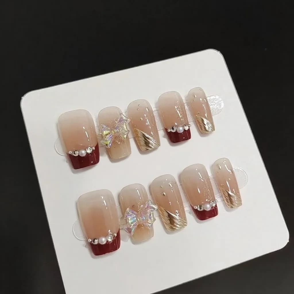 Kurze French-Tip-Künstelnägel mit Goldglitter und Schleifen-Design