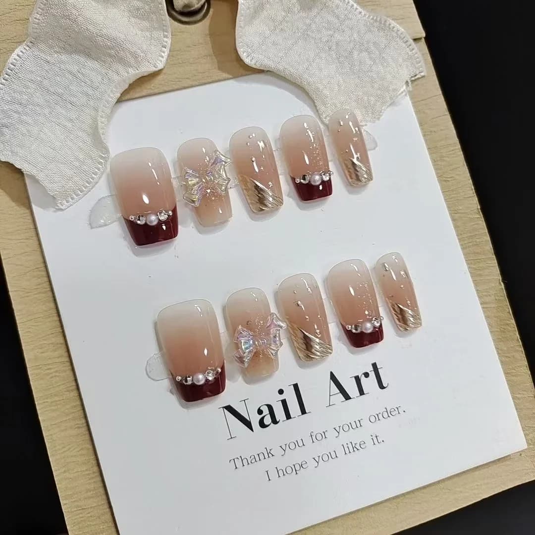 Kurze French-Tip-Kunstnägel mit Goldglitzer und Schleifen-Design